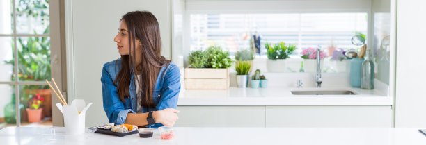 广角图片美丽的年轻女子吃送寿司看向一边，放松的侧面姿势与自然的脸与自信的微笑。图片下载