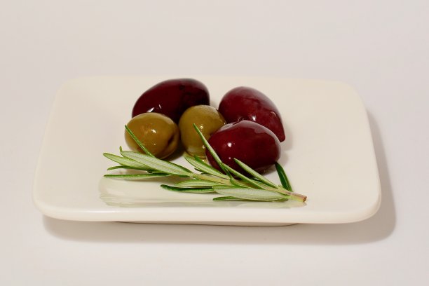 一张黑色和绿色的橄榄和迷迭香叶的特写照片躺在一个小的白色方形盘子上。图片下载