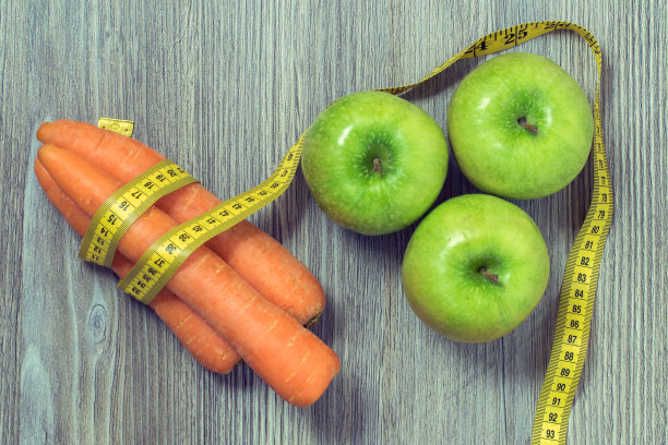 健康营养的概念。俯视图照片绿色的新鲜苹果，美味的胡萝卜和卷尺在木头桌子上图片下载