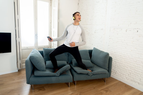 年轻快乐的少年男性在耳机里听音乐，在沙发上唱歌跳舞，在家里玩得很开心。在积极的情感和快乐中，休闲音乐和科技理念。图片下载