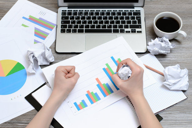 从上面木制的桌子上看，图表，咖啡杯，笔记本电脑和手揉皱的纸图片下载