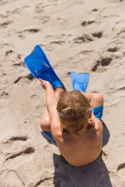 阳光明媚的日子里，快乐的小男孩穿着脚蹼跑进大海。孩子们要去海里游泳。假期。儿童在海滩上的活动。欢乐和幸福。图片下载