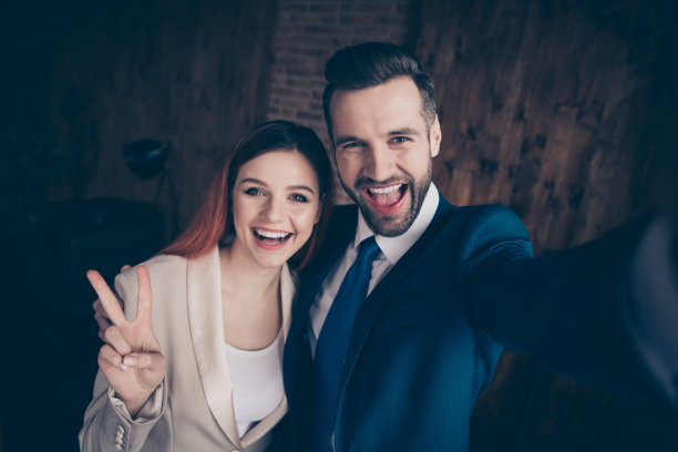 近距离的照片她她的商务女士他他他的男人伙伴手手臂握住智能手机做自拍显示v手势打招呼惊奇地激动地站着办公室穿着正式穿西装图片下载