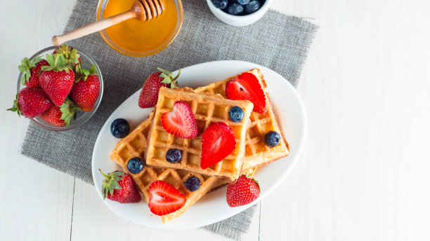 新鲜的自制食物的照片，浆果比利时华夫饼与蜂蜜，巧克力，草莓，蓝莓，枫糖浆和奶油。健康的早餐甜点搭配果汁。图片下载