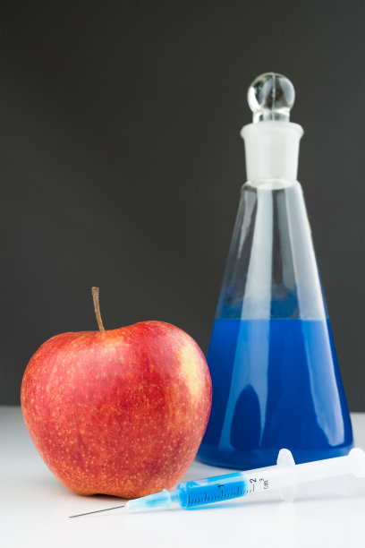 白色的实验桌上放着蓝色液体、苹果和注射器。图片下载