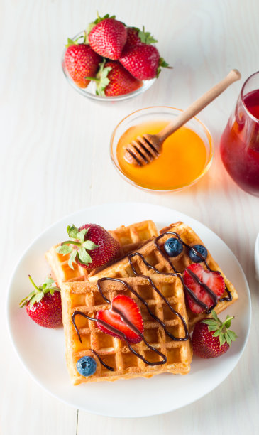 新鲜的自制食物的照片，浆果比利时华夫饼与蜂蜜，巧克力，草莓，蓝莓，枫糖浆和奶油。健康的早餐甜点搭配果汁。图片下载