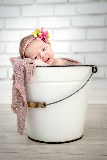 白色珐琅桶内的女婴/婴儿，睁着眼睛，带着粉红色的花头巾。图片下载