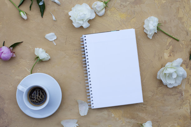 打开笔记本，米色背景上有花和黑咖啡。平的。前视图。副本的空间。图片下载