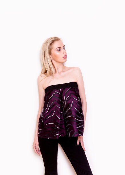 年轻美丽的金发女人穿着性感的衣服紫色的上衣和黑色的裤子在白色的背景图片下载