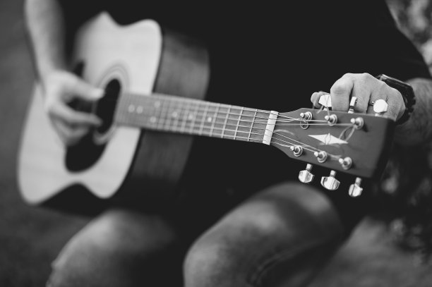 一个吉他手的图片，一个年轻人坐在一个自然的花园里弹吉他，音乐的概念图片下载