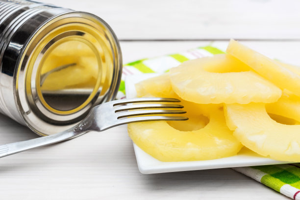 用叉子和锡罐装好菠萝罐头，放在白色的木桌上。图片下载