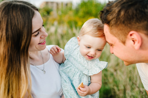 在大自然中拥抱父母的女儿。妈妈，爸爸和蹒跚学步的女孩，走在草地上。快乐的年轻家庭一起度过时光，在户外，度假，户外。家庭度假的概念。图片下载