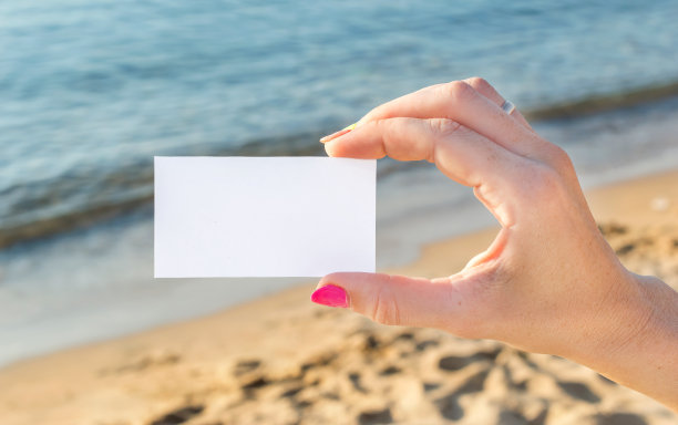 在海边，女人的手握着空白卡片。图片下载