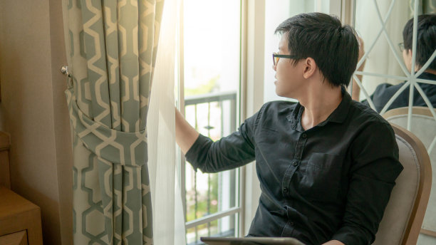 年轻的亚洲商人坐在舒适的卧室的椅子上，用数字平板电脑看窗户。具有现代电子小玩意概念的家居生活方式图片下载