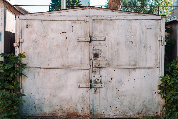 关闭不完全生锈的金属车库门关闭。锁上生锈铁门的纹理损坏。丑的金属表面。粗糙褪色不均匀钢闸门的纹理背景。过时的金属表面。图片下载