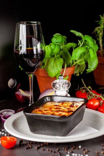 意大利菜的概念。烤千层面放在黑色陶瓷烤盘里。上菜时，厨师在餐厅里装饰这道菜。的背景图片。本空间图片下载