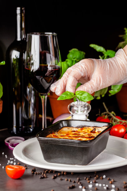 意大利菜的概念。烤千层面放在黑色陶瓷烤盘里。上菜时，厨师在餐厅里装饰这道菜。的背景图片。本空间图片下载