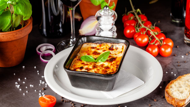 意大利菜的概念。烤千层面放在黑色陶瓷烤盘里。上菜时，厨师在餐厅里装饰这道菜。的背景图片。本空间图片下载