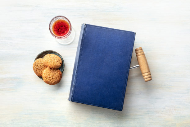 一张照片是一本书的照片，上面有一个用作书签的瓶塞钻，还有一杯带饼干的甜酒，照片的顶部有文字的地方图片下载