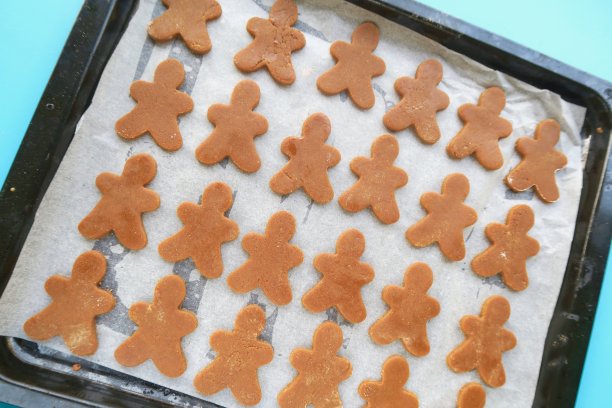 在不粘炉托盘的羊皮纸/防油纸上，用饼干切割器/饼干切割器制作的姜饼面团的家庭烘焙照片，以蓝色背景图片下载