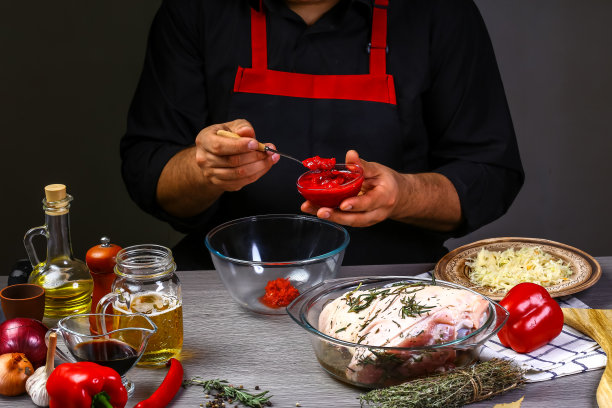 厨师手拿泡菜，在猪蹄上加入辣椒酱，背景为黑色。食物食谱照片，复制文字图片下载