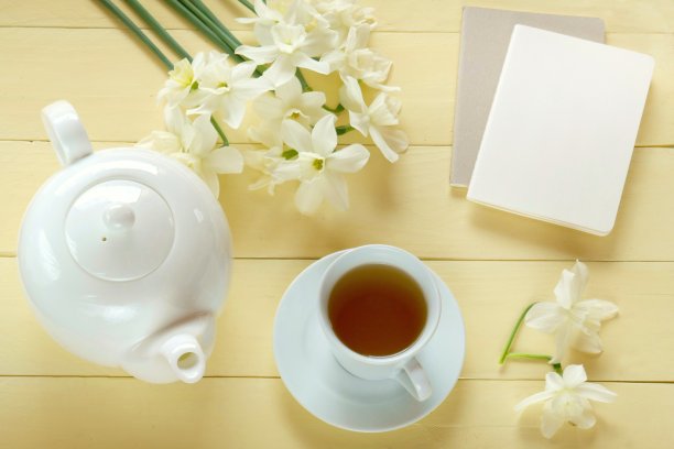 春天的茶。平的。笔记本，白色茶壶，一杯茶，一束白色水仙花在淡黄色的背景。俯视图，复制空间。春天的心情图片下载