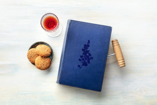 一张照片是一本旧书，上面有一个用来做书签的老式开瓶器，还有一杯带饼干的甜酒，照片是从顶部复制的图片下载