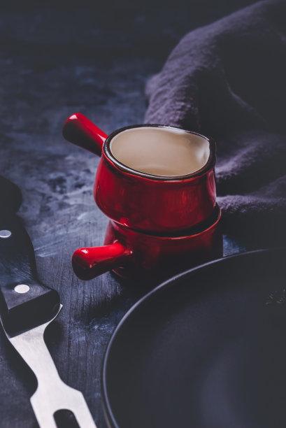 两个杯子的垂直照片。杯子或小碗是饱和的红色，黑色边缘和白色内侧。杯子堆放在一块深色的木板上，旁边是布料。图片下载