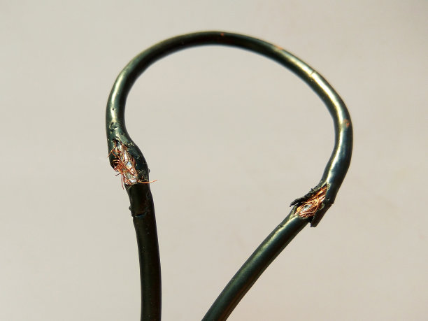 灯光背景上损坏的黑色电线。危险破损电力电缆图片下载