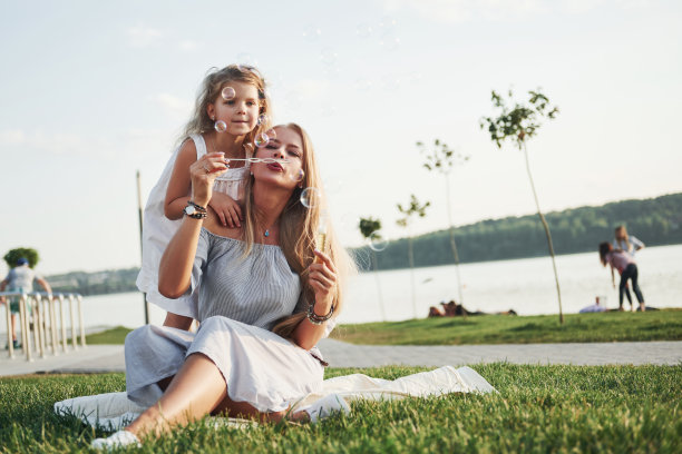 一个可爱的小女孩和她的妈妈在公园里吹泡泡。图片下载