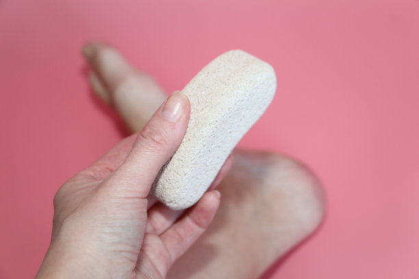 在照片中，一个女人的手拿着她脚后跟附近的浮石。图片下载