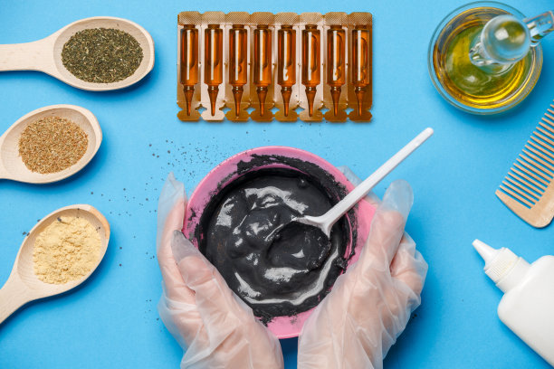 从上面的照片，粉红色的杯子与黑色粘土，面膜油，木制勺子，梳子，人的手与勺子图片下载