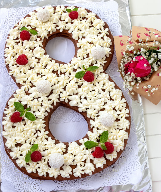 白色奶油乳酪、覆盆子和椰子糖装饰的8字形大蛋糕。生日快乐或3月8日妇女节概念，顶部视角，白色木质背景图片下载