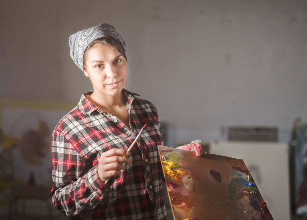 艺术家在她的工作室，穿着衬衫，拿着一把刷子。图片下载