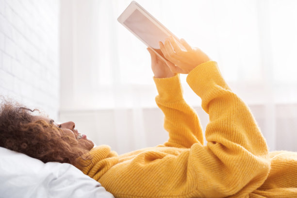 快乐女孩用着平板电脑，躺在床上图片下载