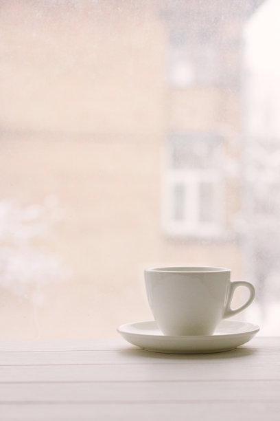 在房子和下雪的天气背景下，窗台上的白色杯子。颗粒效应，作者处理。图片下载