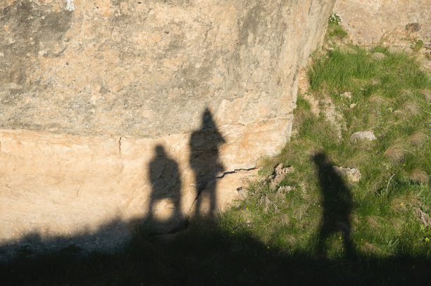 三个旅行者朋友的影子在绿草旁边的黄色岩石上图片下载