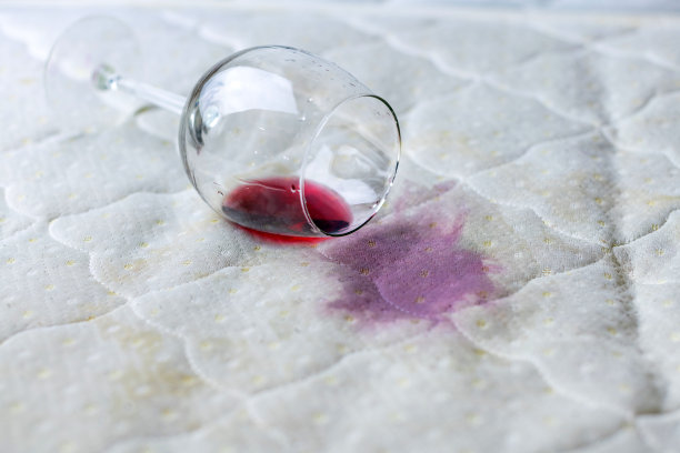 酒杯洒在床上。酒杯掉在白床单上。粉红色的湿斑。不幸,不幸的情况。图片下载