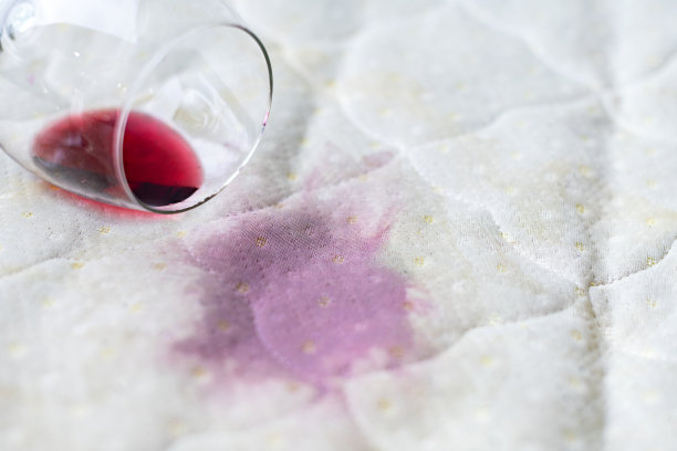 酒杯洒在床上。酒杯掉在白床单上。粉红色的湿斑。不幸,不幸的情况。图片下载
