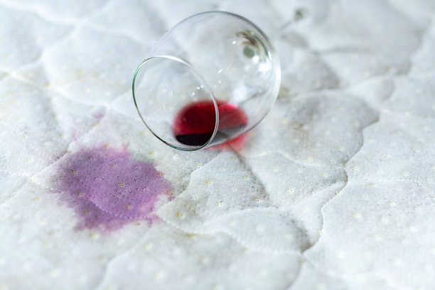 把酒杯洒在床上了。不小心把酒杯掉在了白色的床单上。不幸,不幸的情况。湿的污点。图片下载