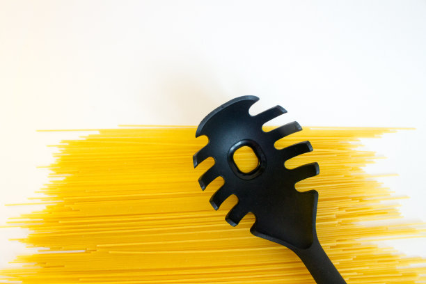 长长的黄色生意大利面，黑色塑料勺子，白色勺子上有孤立的小孔图片下载