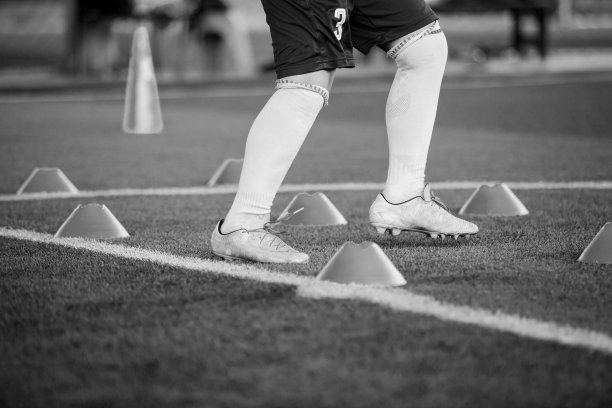 足球运动员慢跑和跳跃的黑白图片之间的圆锥体标记在绿色人造草皮上进行足球训练。图片下载