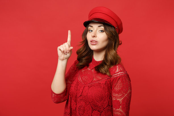 肖像的自信的年轻女子在蕾丝连衣裙，cap holding食指向上与伟大的新想法孤立在明亮的红色墙背景。人真诚情感，生活理念。模拟拷贝空间。图片下载