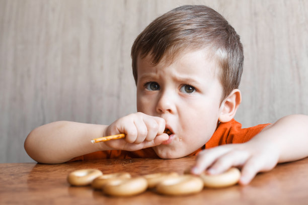 可爱的男孩吃着松脆的稻草。小男孩坐在木桌旁图片下载