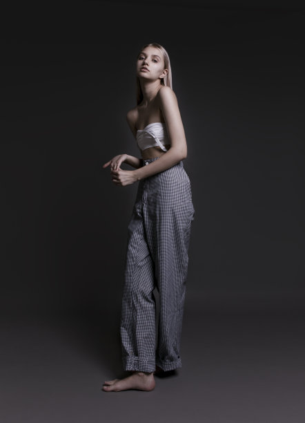 美丽的年轻女子穿着黑白格子宽裤子和白色运动胸罩摆姿势在黑色的背景图片下载