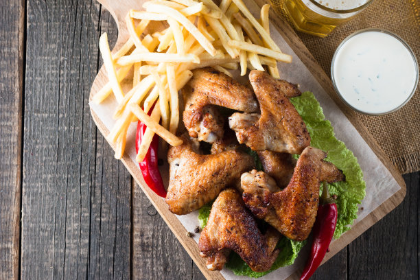 烧烤鸡翅与薯条和啤酒的特写照片。烤肉配酱汁，番茄酱，蛋黄酱。快餐和垃圾食品的概念。图片下载