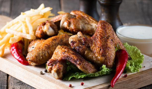 烧烤鸡翅与薯条和啤酒的特写照片。烤肉配酱汁，番茄酱，蛋黄酱。快餐和垃圾食品的概念。图片下载