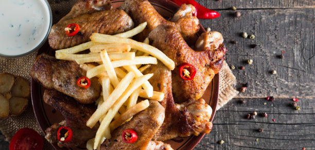 烧烤鸡翅与薯条和啤酒的特写照片。烤肉配酱汁，番茄酱，蛋黄酱。快餐和垃圾食品的概念。图片下载