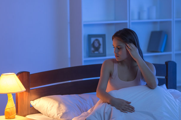 头疼的女人坐在床上。晚上的时间图片下载