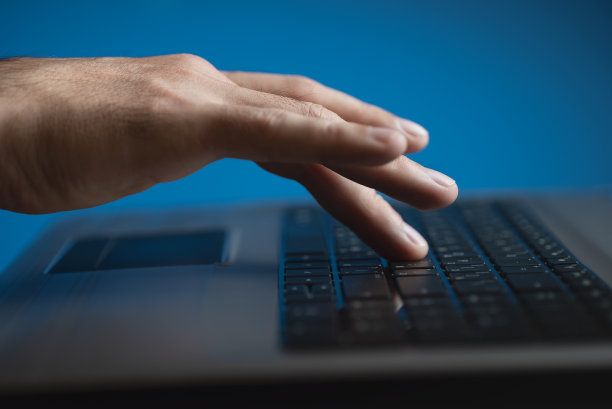 男人的手和笔记本电脑键盘。蓝色背景图片下载